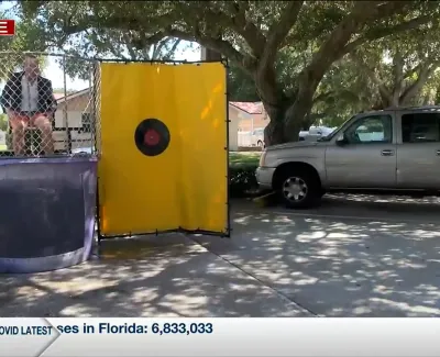 Man stands near a dunk tank at an outdoor event with a tree and parked car in the background.