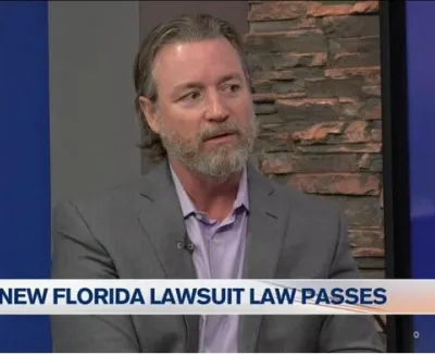 Man in gray suit discussing the new Florida lawsuit law during a televised interview segment.