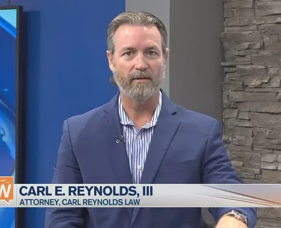 Attorney Carl E. Reynolds III speaking on Suncoast View with studio background and news ticker.