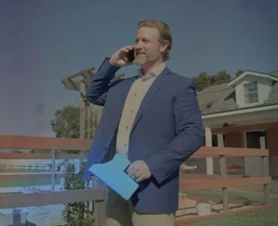 Man in blue blazer talking on phone outside house next to wooden fence on sunny day