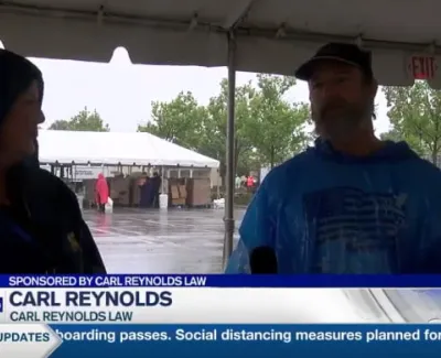 Two people wearing rain ponchos under a tent during a rainy outdoor event with law firm sponsorship banner.