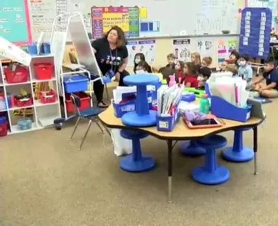 Teacher reading to young students sitting on carpet in a colorful elementary classroom with educational materials