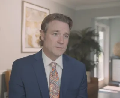 Attorney Carl Reynolds in a blue suit speaking in a professional office setting with artwork and plants