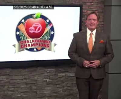 Two news anchors standing beside a screen displaying ABC 7 Chalkboard Champions logo with award iconography.