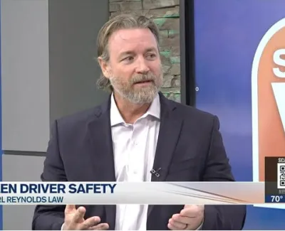 Man in suit discussing teen driver safety laws during a news segment with studio background and lower third text.