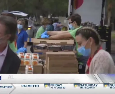 Volunteers wearing masks packing food boxes at an outdoor community food distribution event.
