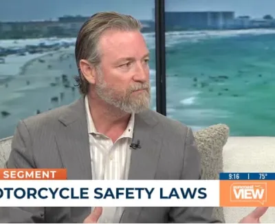 Man in gray suit discussing motorcycle safety laws on Bay news segment with beach backdrop.