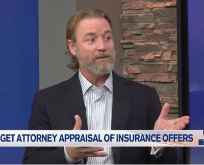 Male attorney discussing insurance offer appraisals on a news segment with studio background and graphics.