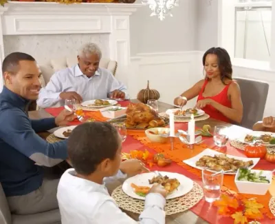 Multi-generational family enjoying a Thanksgiving meal with turkey and autumn decorations at the dining table.