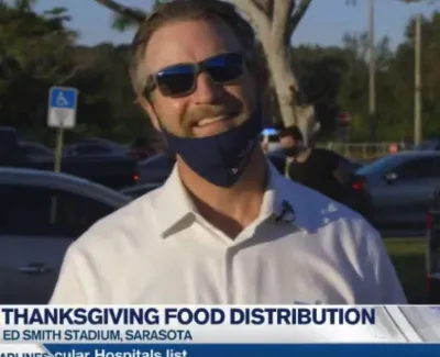 Man wearing sunglasses and a mask smiling outdoors at Thanksgiving food distribution event in Sarasota.