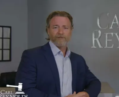 Man in navy suit standing in modern law office with Carl Reynolds Law sign on wall.