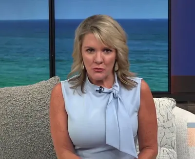 Blonde female news anchor in a light blue sleeveless top speaking on a studio set with ocean background.