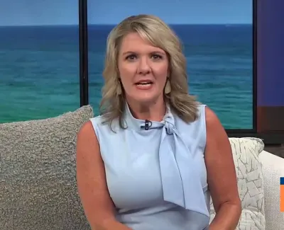 Woman in light blue sleeveless blouse hosting Suncoast View with ocean background and weather info on screen
