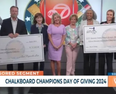 Group of people on TV show holding large donation checks for Chalkboard Champions Day of Giving 2024 event