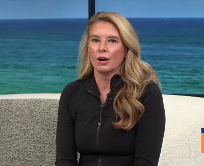 Blonde woman with long hair speaking on a talk show set with ocean background and Suncoast View logo.