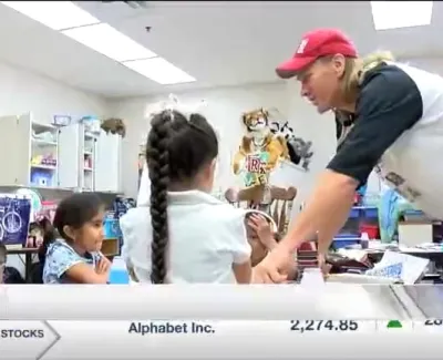 Teacher in red cap engaging with young students in a colorful classroom setting with educational posters.