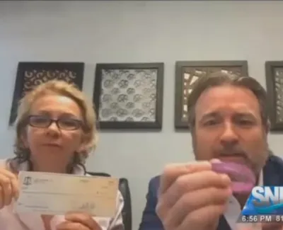 Two people in an interview showing a check and a pink object with SNN logo on screen corner