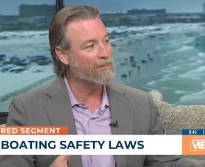 Man in suit discussing boating safety laws on a live TV segment with beach background visible through window