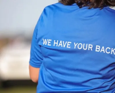 Person in blue shirt with We Have Your Back text on the back in an outdoor setting with blurred background.