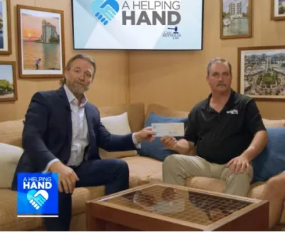 Three men sit on a couch exchanging a check for community support labeled A Helping Hand.