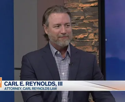 Attorney Carl E. Reynolds III in a suit during a Suncoast View TV interview with a stone wall background.