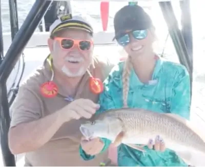 Two anglers on a boat proudly holding a large fish caught during a sunny day on the water.
