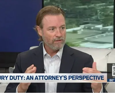 Attorney discusses jury duty perspective during a televised interview on a white couch with city view background