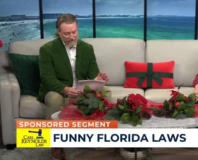 Two hosts discussing funny Florida laws on a holiday-themed TV talk show set with ocean backdrop.