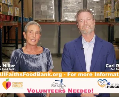 Two people speaking in a food bank warehouse with volunteer information banners visible