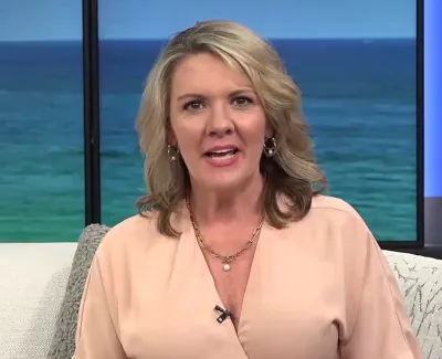 Blonde woman in peach blouse speaking on a set with ocean and blue background behind her