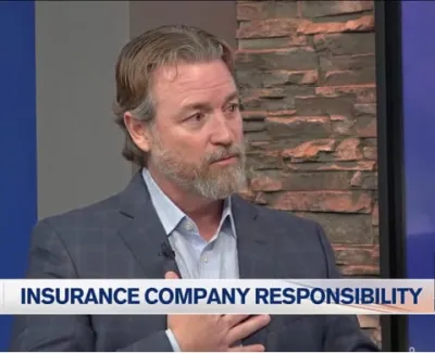 Man in suit discussing insurance company responsibility on local news with stone background and logo.