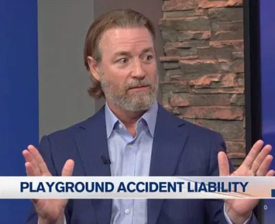 Man in blue suit discussing playground accident liability on news broadcast set.