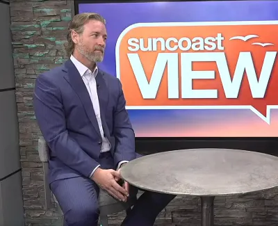 Two hosts seated at a round table discussing on the Suncoast View TV show set with logo and time visible