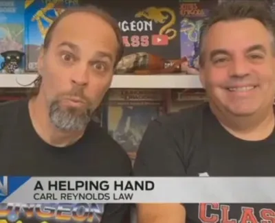 Two men smiling in front of a shelf with games and collectibles, caption reads A Helping Hand Carl Reynolds Law.