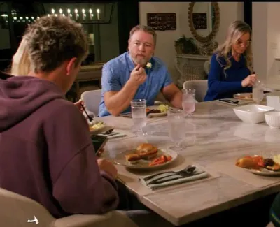 Family and friends sharing a meal at a modern kitchen dining table with plates of food and drinks.