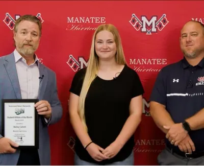Three people standing in front of Manatee Hurricanes backdrop holding Student Athlete of the Month award.