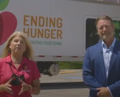 Two people standing in front of an Ending Hunger Faiths Food Bank truck outdoors during the day.