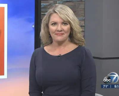 Female news anchor in blue dress standing by a large graphic board with 'Let Raw' text in a studio setting.