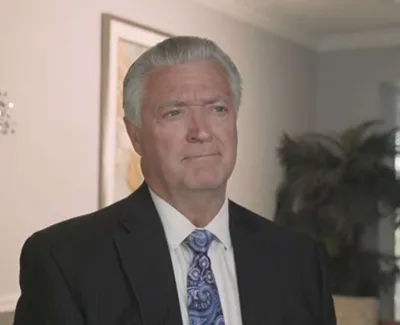 Mature businessman with gray hair wearing a suit and paisley tie in a professional office setting.
