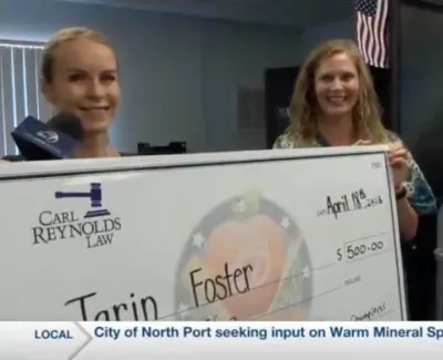 Two women holding large check for $500 from Carl Reynolds Law to Tarin Foster, indoor setting with American flag