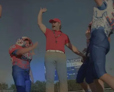 Football coach celebrating with young players during a daytime outdoor practice or game.