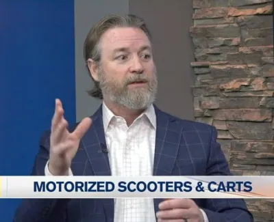 Man in a blue checkered suit discussing motorized scooters and carts on TV news segment