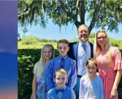 Family of six smiling outdoors under a large tree with Spanish moss on a sunny day.