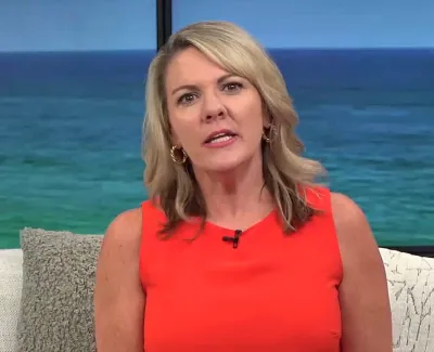 Woman in red sleeveless top speaking on a couch with ocean view background and cushions.