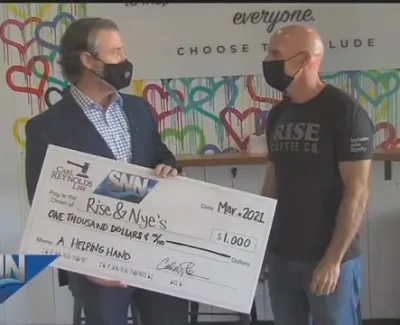 Two men wearing masks hold a $1,000 check for Rise & Nye's at a colorful community event