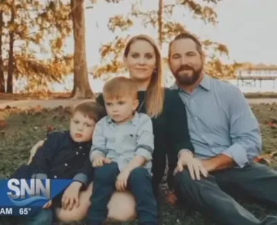 Family of four sitting on grass near lake with trees and dock in the background on a sunny day