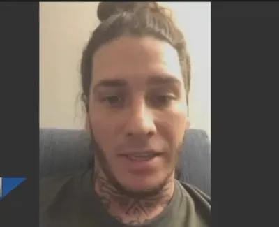 Close-up of a man with neck tattoos speaking in a video call with SNN news logo and time display.