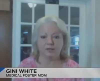Medical foster mom Gini White speaking during a video interview in a home setting with cabinet and window in background
