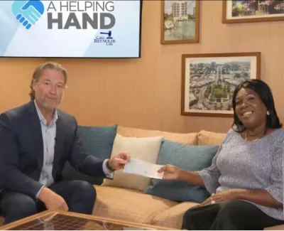 Man in suit handing check to smiling woman on couch with framed art and A Helping Hand sign behind