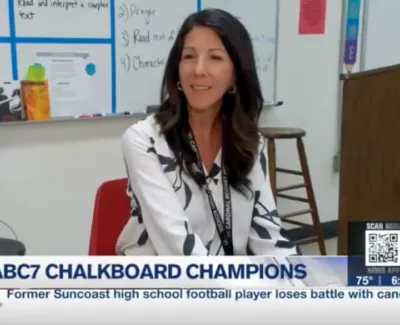 Female teacher sitting in classroom with educational materials and whiteboard visible in background